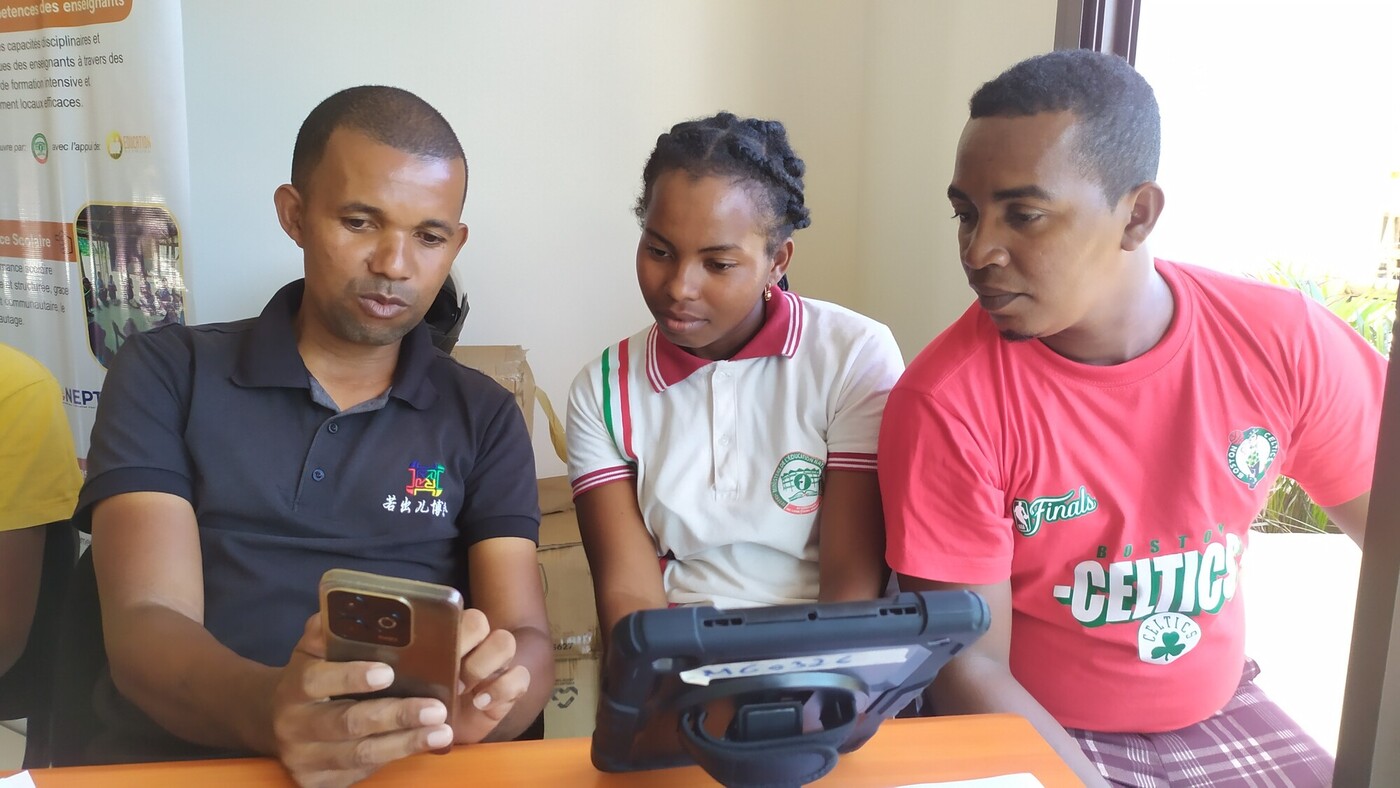 A man shows something on his phone screen to a young woman and young man.