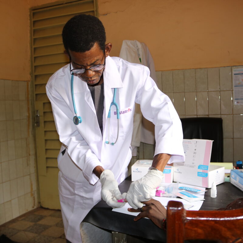 A health worker in a white lab coat touches a patient's hand.
