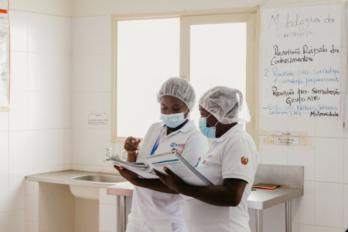 Two nurses review a clipboard while speaking to each other.