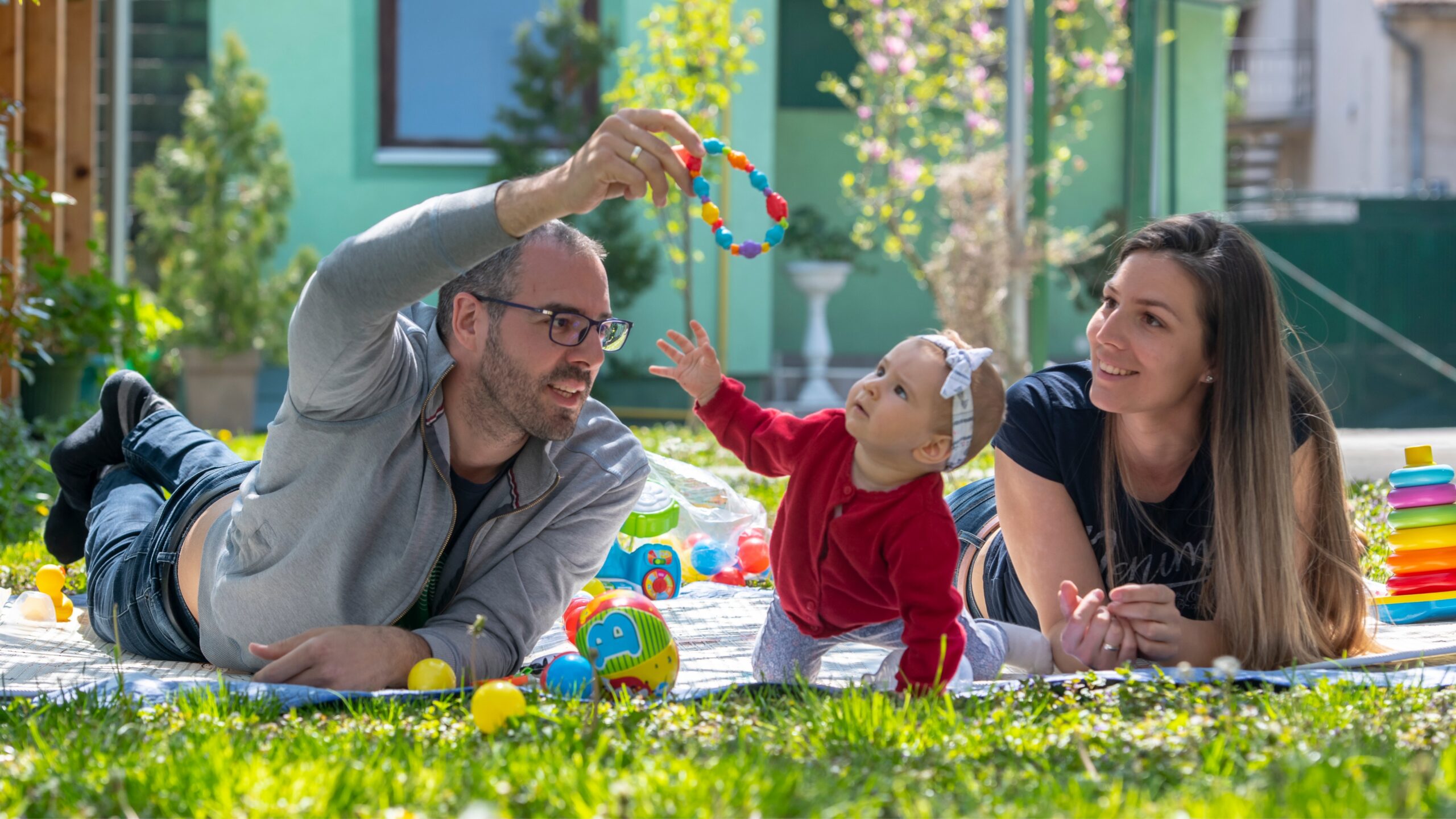 Parents in Serbia play with their child on a blanket outdoors in the sunshine as part of a playful parenting learning experience.