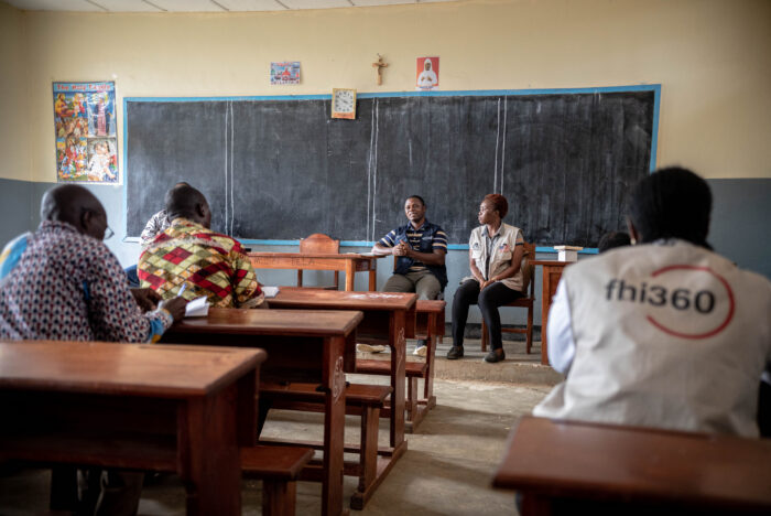 Two people sit in chairs at the front of a classroom during a training.