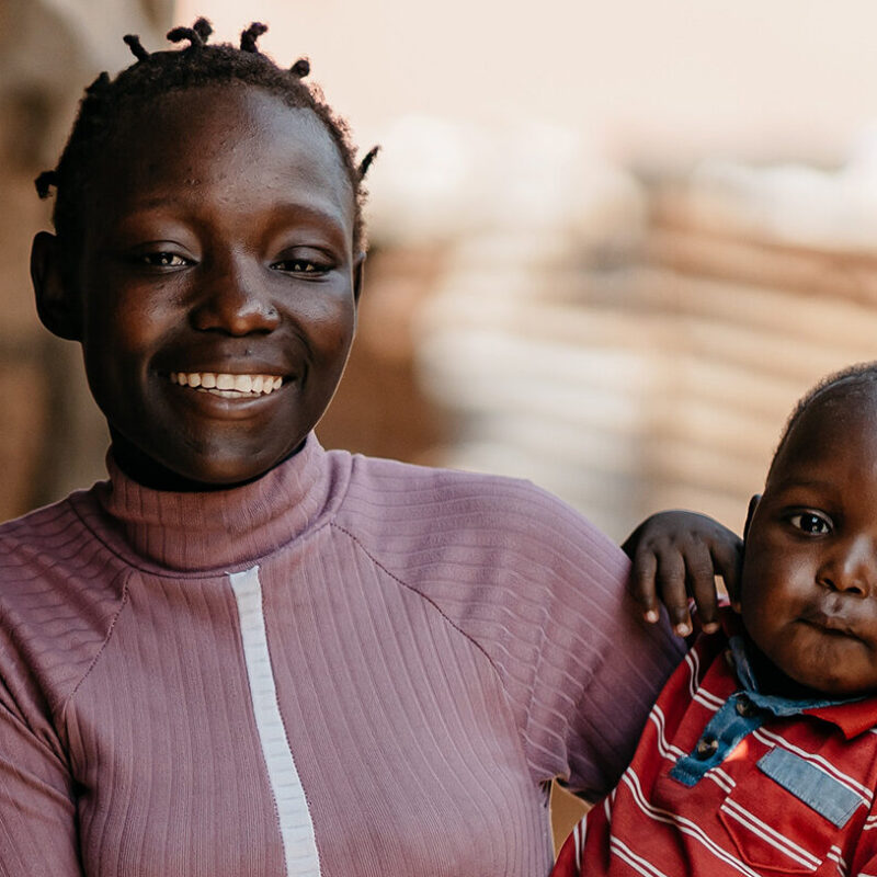 A smiling woman holds a baby on her hip.