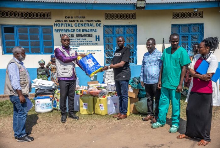 Seven people pose in front of a hospital holding kits.