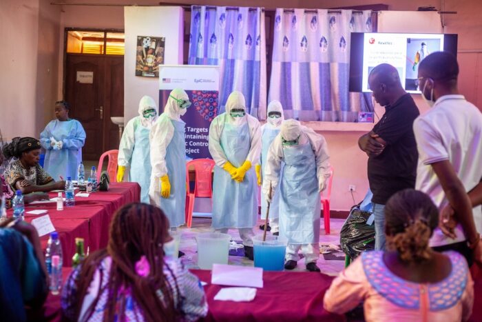 Six people wearing PPE gear during a demonstration while a small crowd watches.