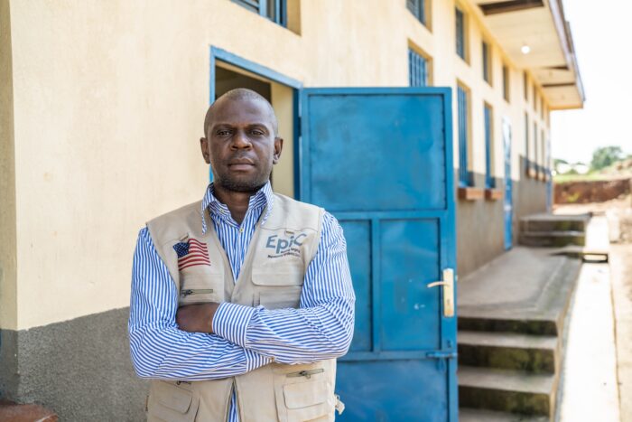 A man, Marien, stands in front of a building with arms crossed.