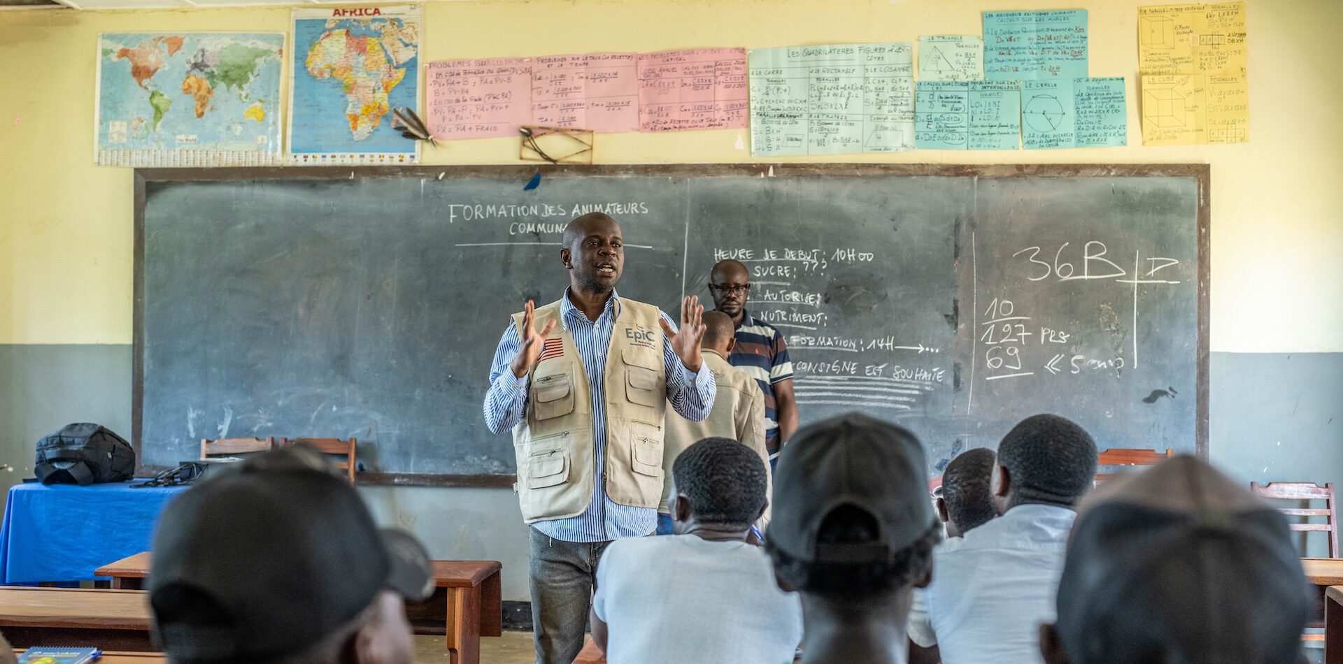 A man, Marien, stands in front of a chalkboard instructing a classroom of people.