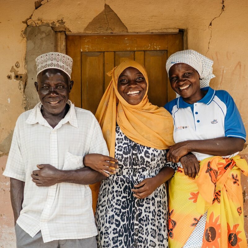 A man and two women, all smiling, standing in front of a door.