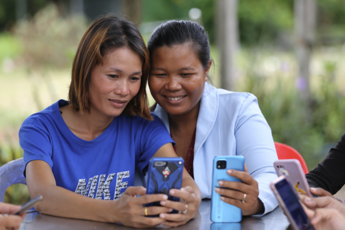 Two women smile as they look at a mobile device.