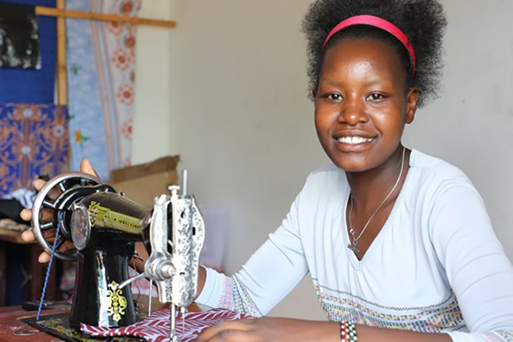 Having practical skills can help reduce vulnerability to HIV exposure. The EpiC project developed economic strengthening hubs in Shinyanga, Tanzania, to teach adolescent girls and young women skills such as tailoring and computer literacy. Here, an adolescent girl named Eva smiles while working at a tailoring mart using skills she learned from EpiC. In addition to teaching skills, the hubs create a platform for participants to receive HIV services. FHI 360 is the lead implementer for EpiC, which is funded b